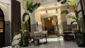 A spacious interior with a high ceiling, ornate wall patterns, and a central seating area with chairs and tables. - Riad citronnier (Fès)