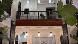 A spacious interior with a high ceiling, ornate wall tiles, and a balcony with wrought iron railings. - Riad citronnier (Fès)