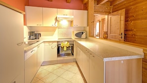 A compact kitchen with white cabinets, a built-in oven, and a microwave. - Feriendorf Wildschonau -cozy Escape (Wildschönau)