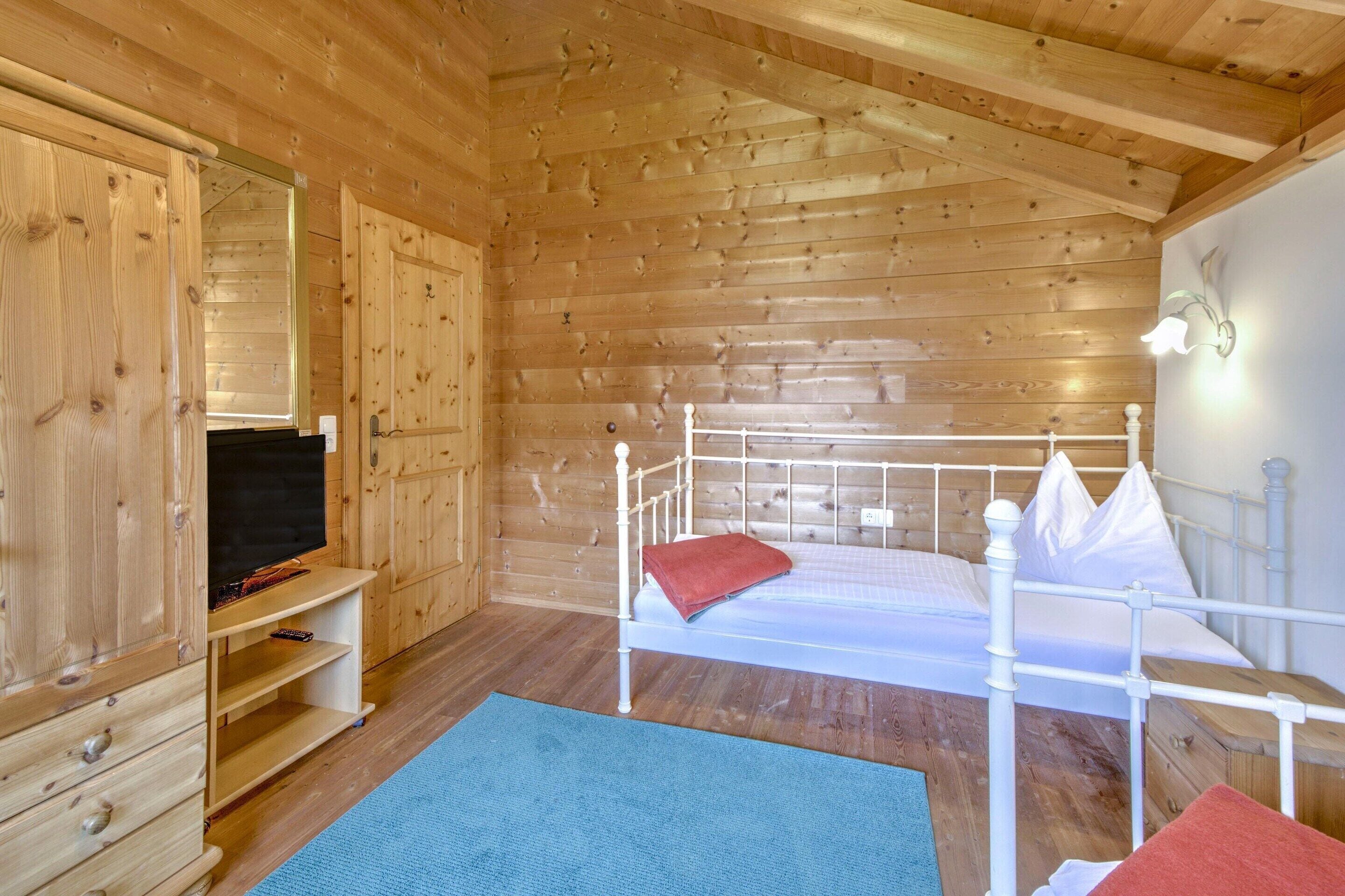 Una camera in una baita di legno con un letto, una televisione su un mobile e un armadio.
