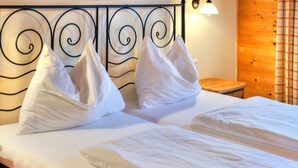 A bed with white linens and pillows, a wooden nightstand, and a metal headboard with a spiral design. - Feriendorf Wildschonau Near Sauna (Wildschönau)