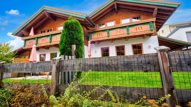 A traditional chalet with a wooden facade, a sloped roof, and a balcony with a pink umbrella. - Feriendorf Wildschonau Near Sauna (Wildschönau)
