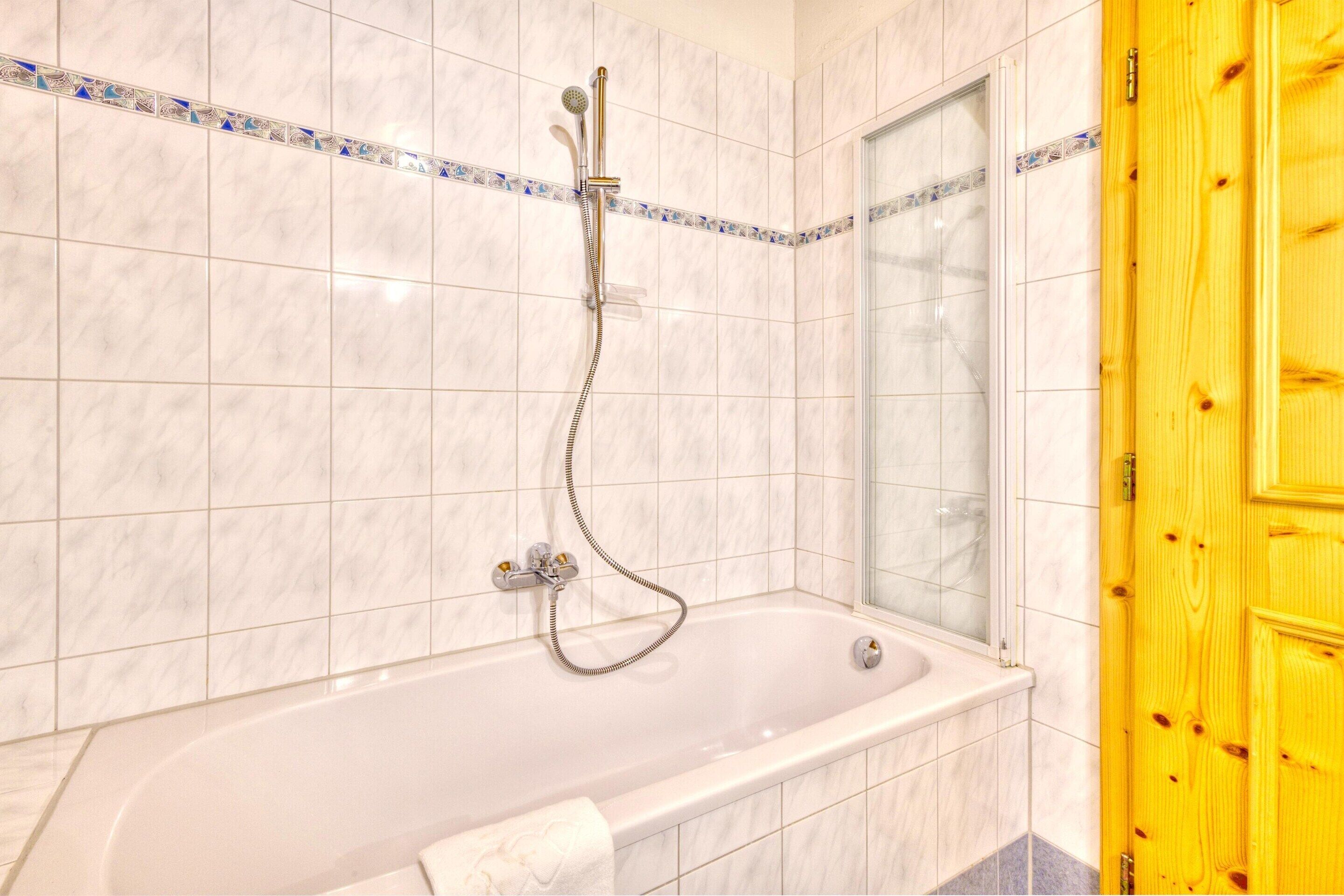 A bathroom with a white bathtub, a showerhead, and a wooden door.