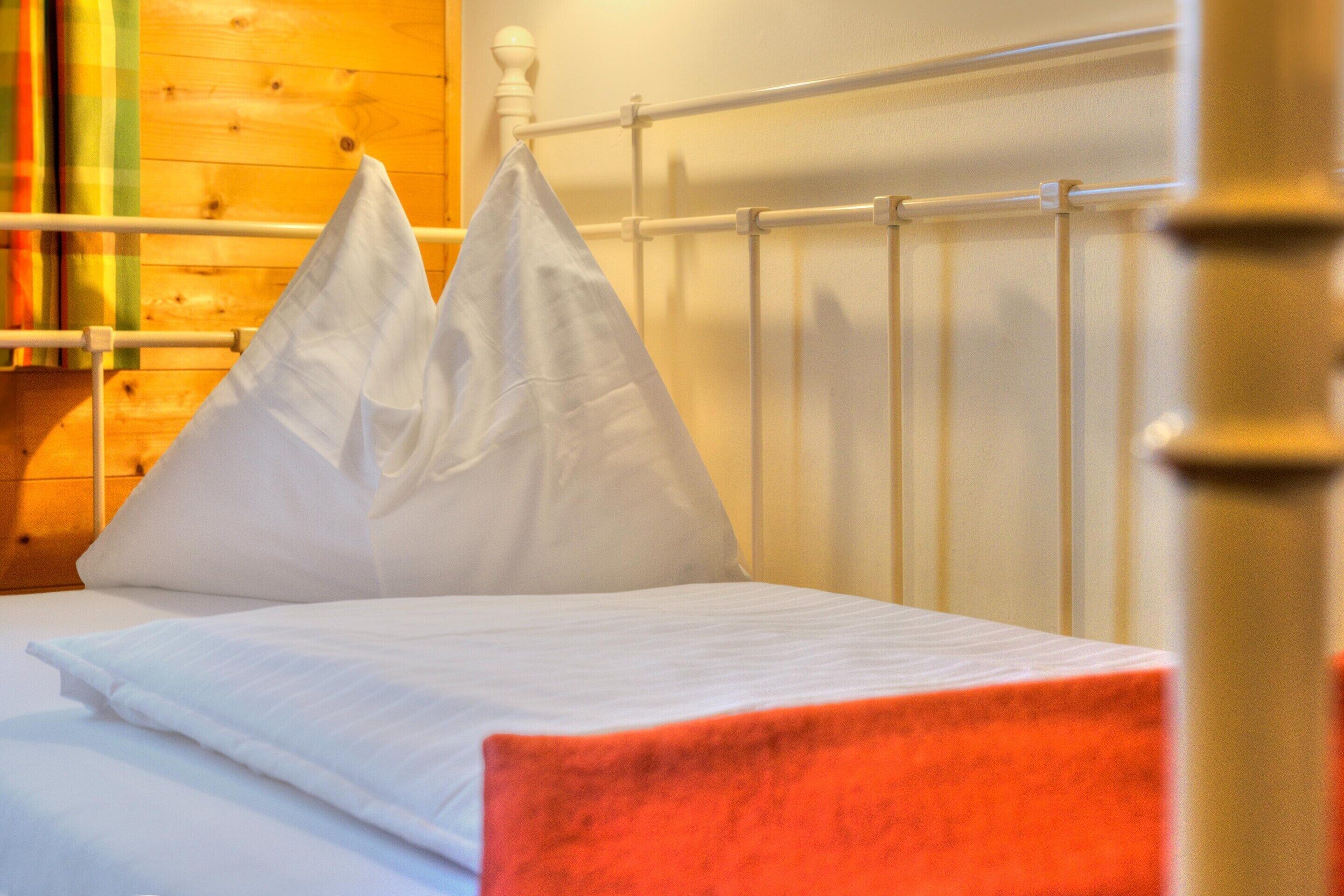 Ein Bett mit weißer Bettwäsche, zwei weißen Kissen, einem Holzkopfende und einem Metallgeländer.