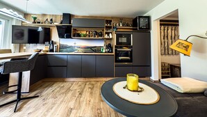 Et moderne køkken med en stor ø, integreret hårde hvidevarer og et spiseområde med udsigt til et naturskønt landskab.