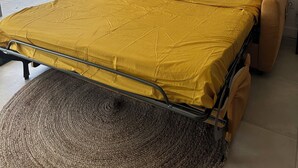 Ein Bett mit gelber Bettdecke, ein großes Spiegel darüber und Blick ins Freie durch eine Schiebetür.
