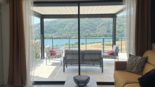 Ein modernes Wohnzimmer mit einer Couch, einem Couchtisch und Blick auf einen See und Hügel durch große Glastüren.