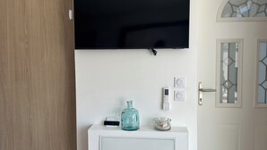 Ein Zimmer mit einer weißen Kommode, einem wandmontierten Flachbildfernseher, einer Holztür und einer Glastür mit geometrischem Muster.