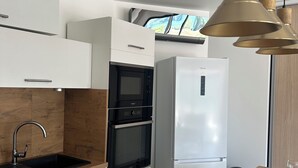 Eine moderne Küche mit weißen Schränken, einer schwarzen Spüle, einem Edelstahl-Wasserhahn und einem eingebauten Backofen. Es gibt einen weißen Kühlschrank und einen Holztisch mit einer Blumenkorb-Dekoration.