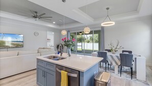 Une cuisine moderne avec un îlot central, un coin repas avec une table et des chaises, un canapé et un ventilateur de plafond.