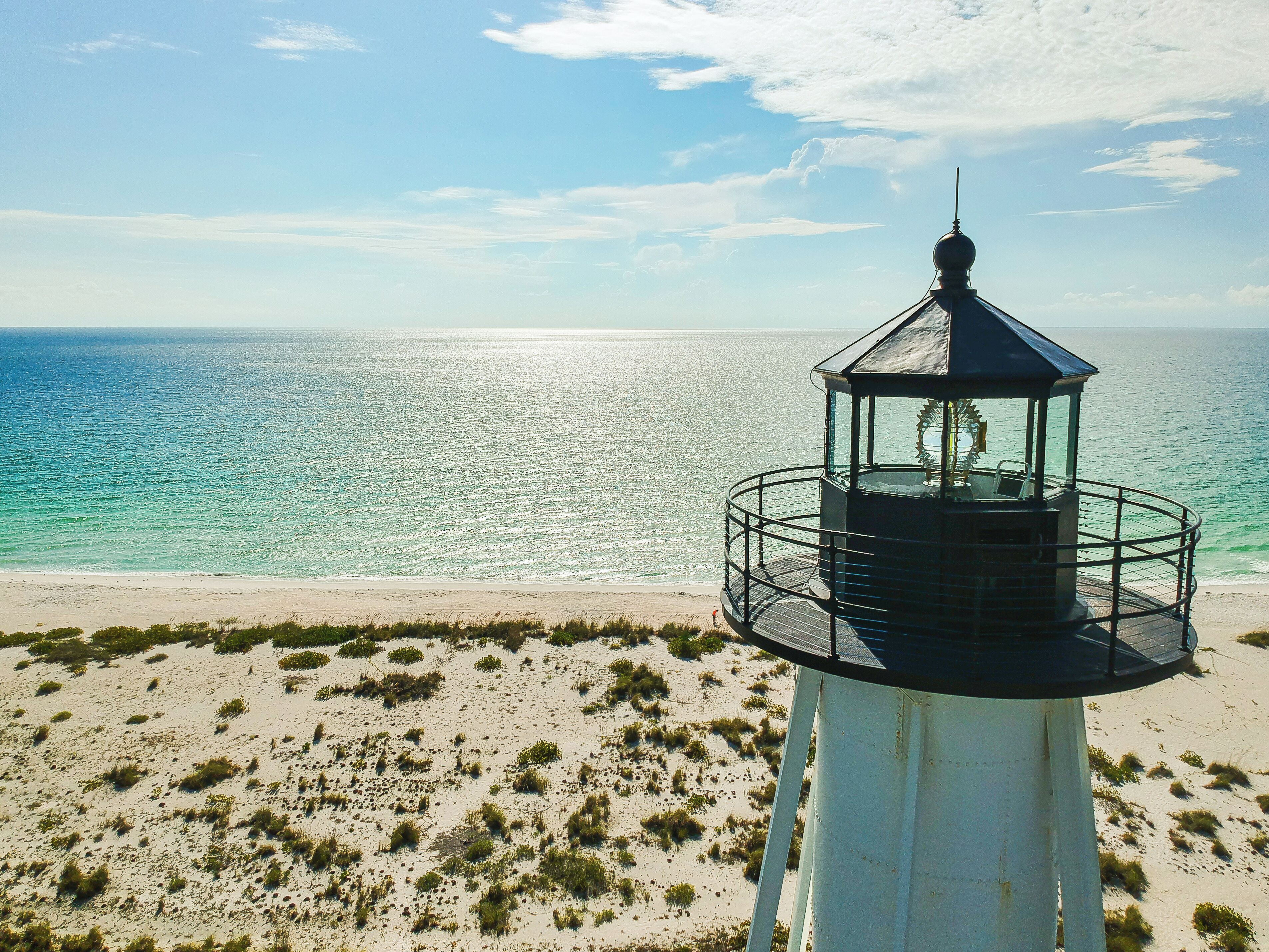 Un faro con una plataforma circular de observación, situado en una playa arenosa con vegetación escasa.
