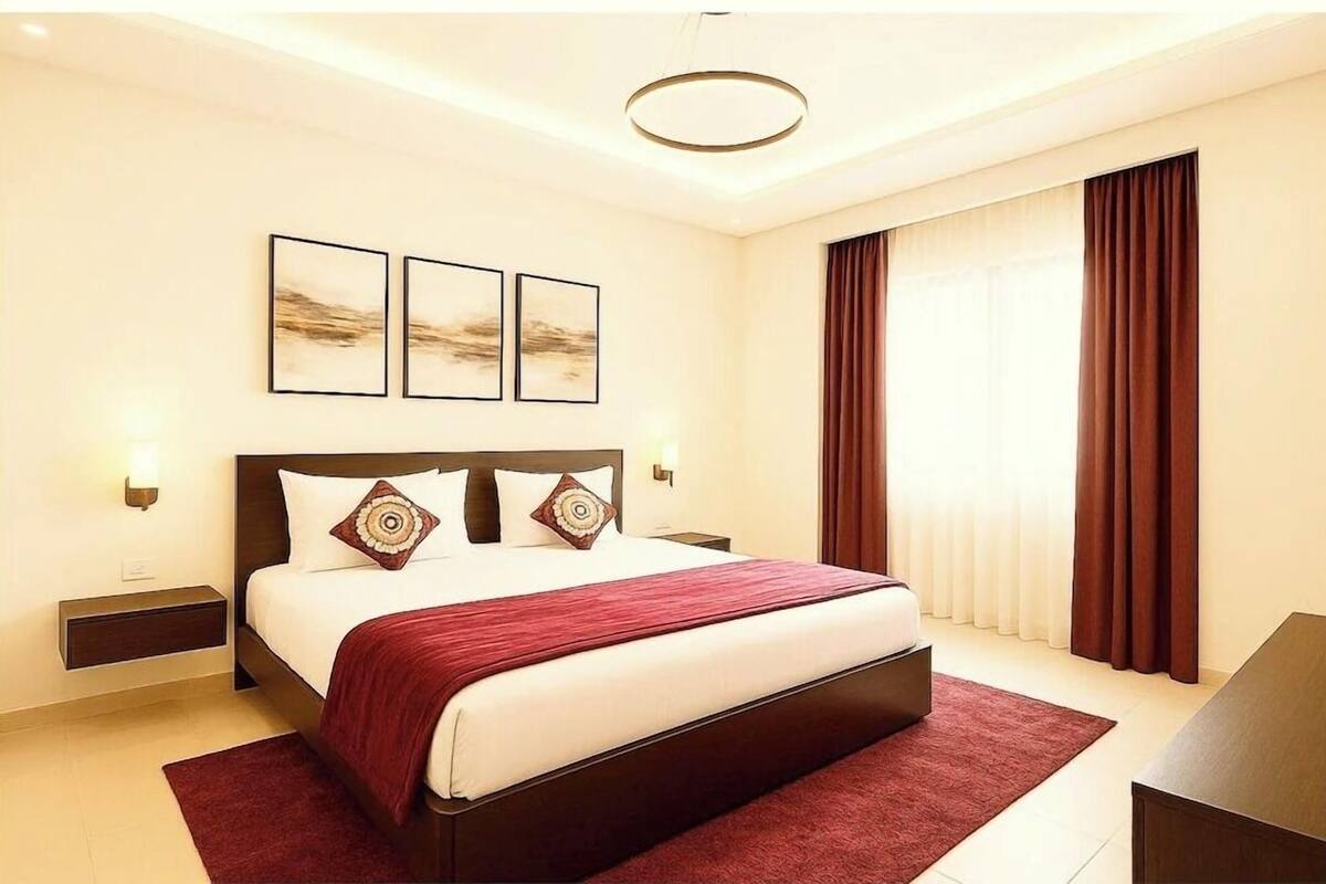 A hotel room with a large bed, two bedside tables, a red rug, and a large window with curtains.