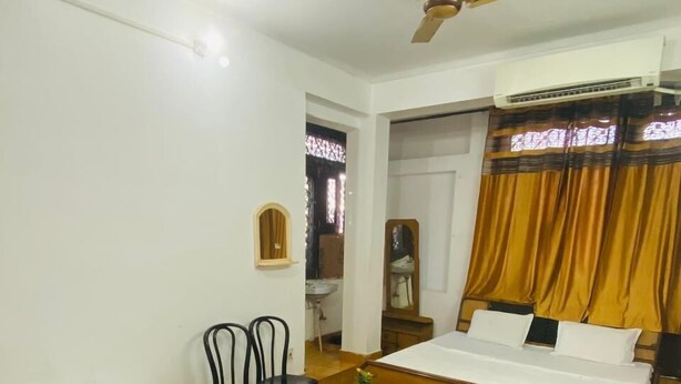 A hotel room with two single beds, a small table, two chairs, a ceiling fan, and a window with curtains. - Prashant Residency (Haridwar)