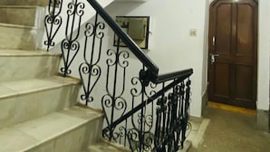 A staircase with ornate black railings and beige steps, leading to a room with a wooden door and a window with patterned curtains. - Prashant Residency (Haridwar)