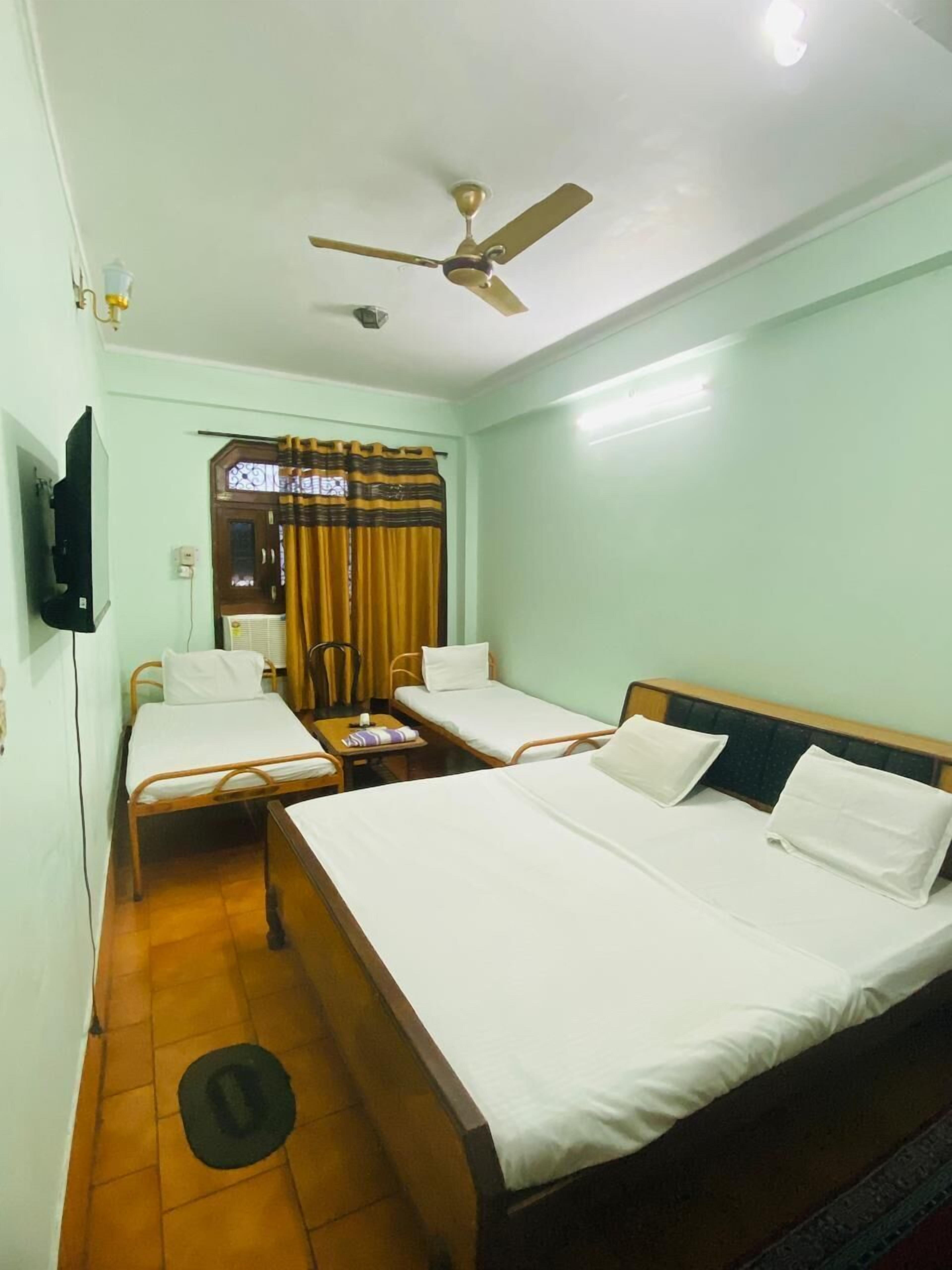 A hotel room with two single beds, a ceiling fan, a TV mounted on the wall, and a window with curtains.