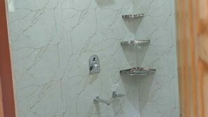 A bathroom with a toilet, a shower with a handheld showerhead, and a water heater. - Prashant Residency (Haridwar)