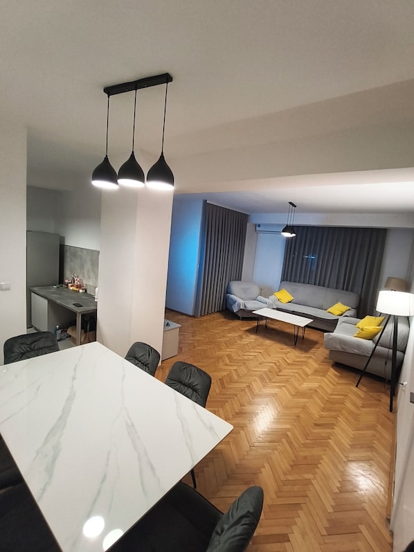 A modern living room with a dining area, a sofa set, and a kitchen in the background.