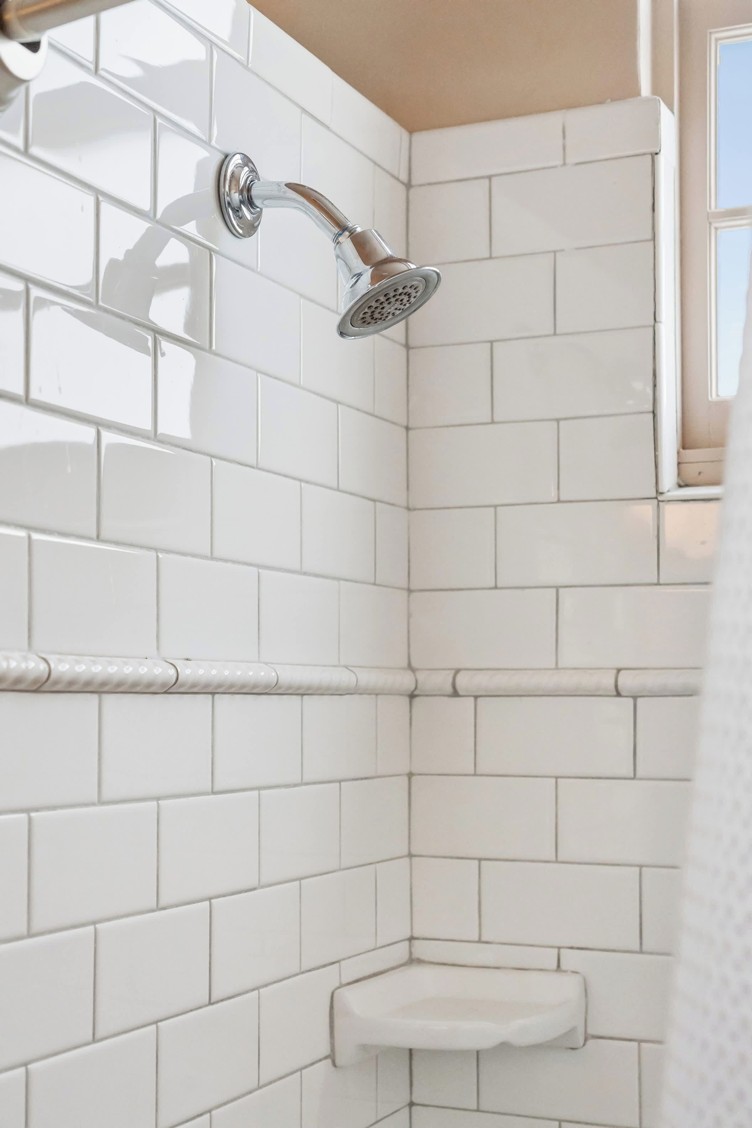 A corner of a bathroom with white tiled walls and a shower area.