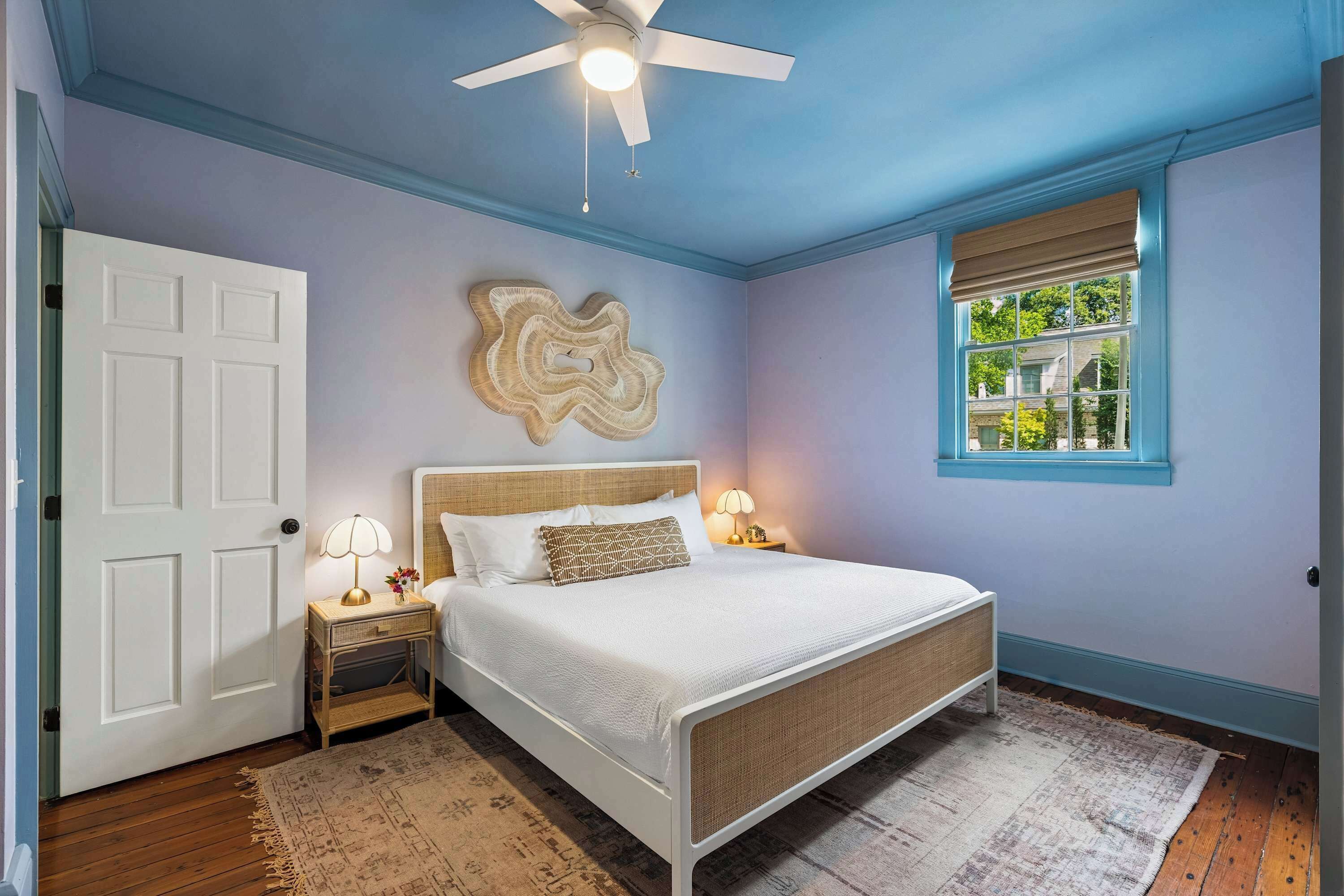 A bedroom with a bed, nightstand, lamp, ceiling fan, and a window with blinds.