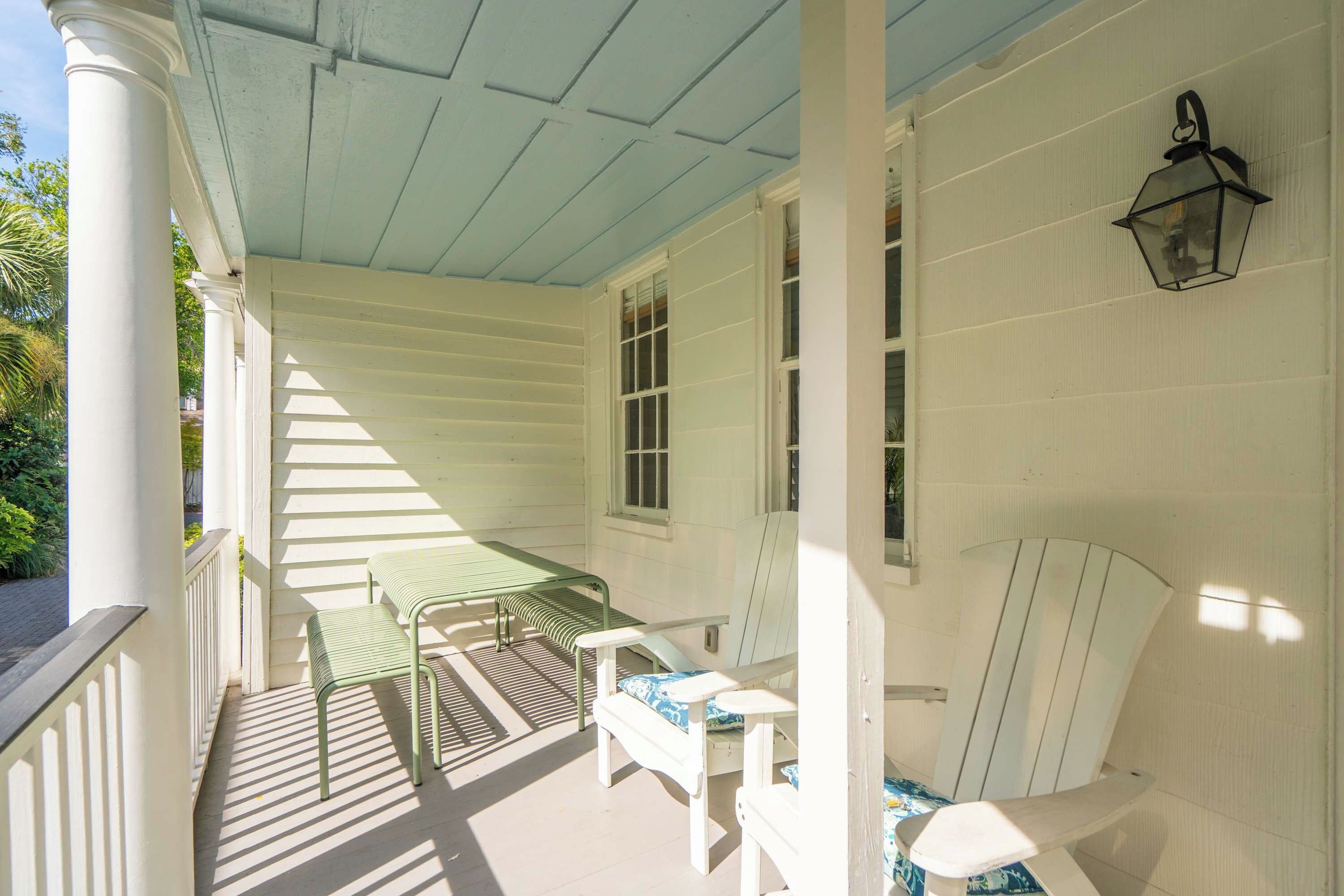 A porch with a bench, a table, and a wall-mounted lantern.