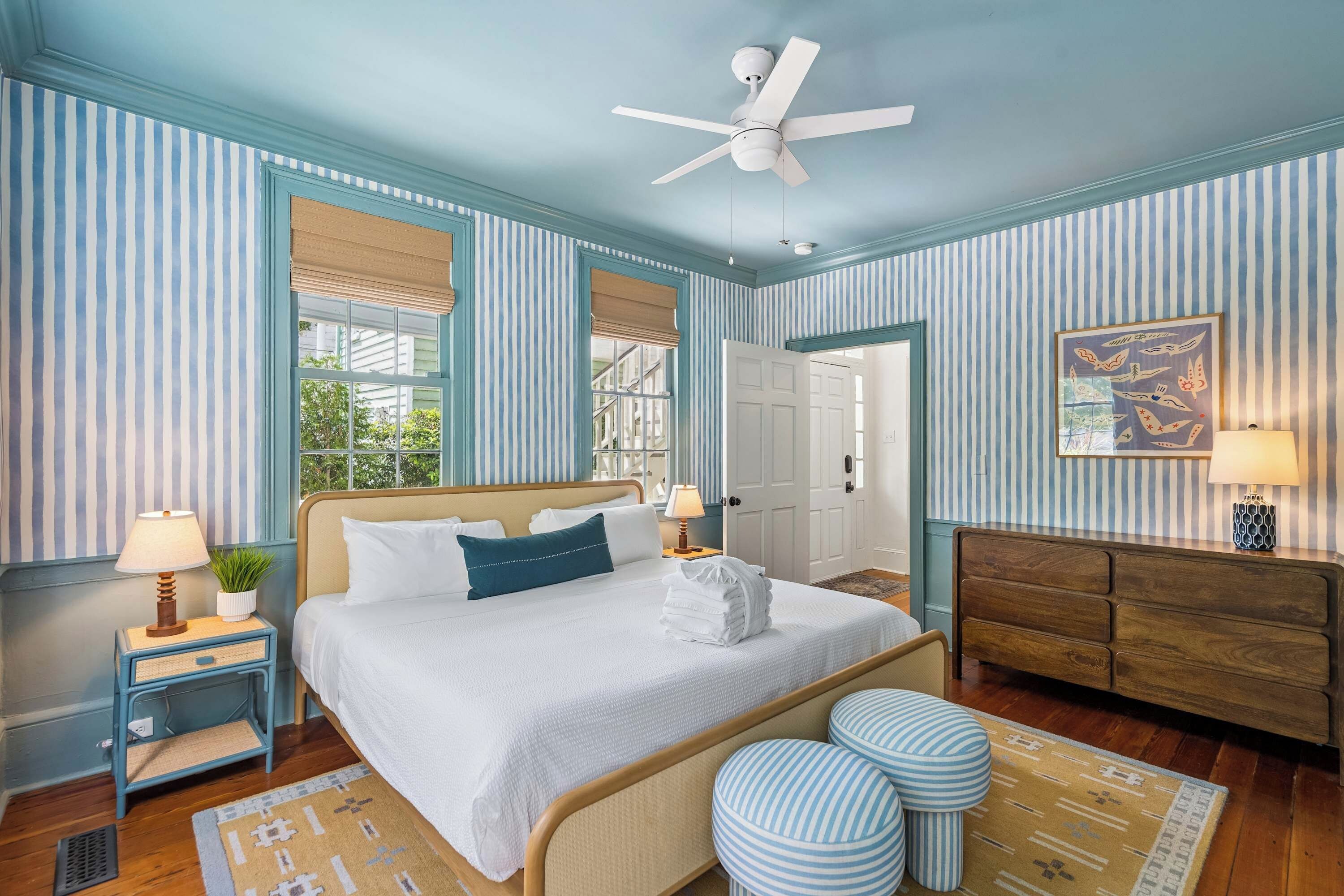 A hotel room with a bed, bedside tables, a ceiling fan, a door, a wall-mounted lamp, and a rug.