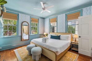 A bedroom with a bed, bedside tables, a ceiling fan, and a large window with a view of greenery.