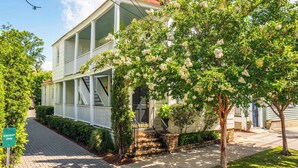 Een tweelaags huis met een veranda, een trap en een boom met witte bloemen.