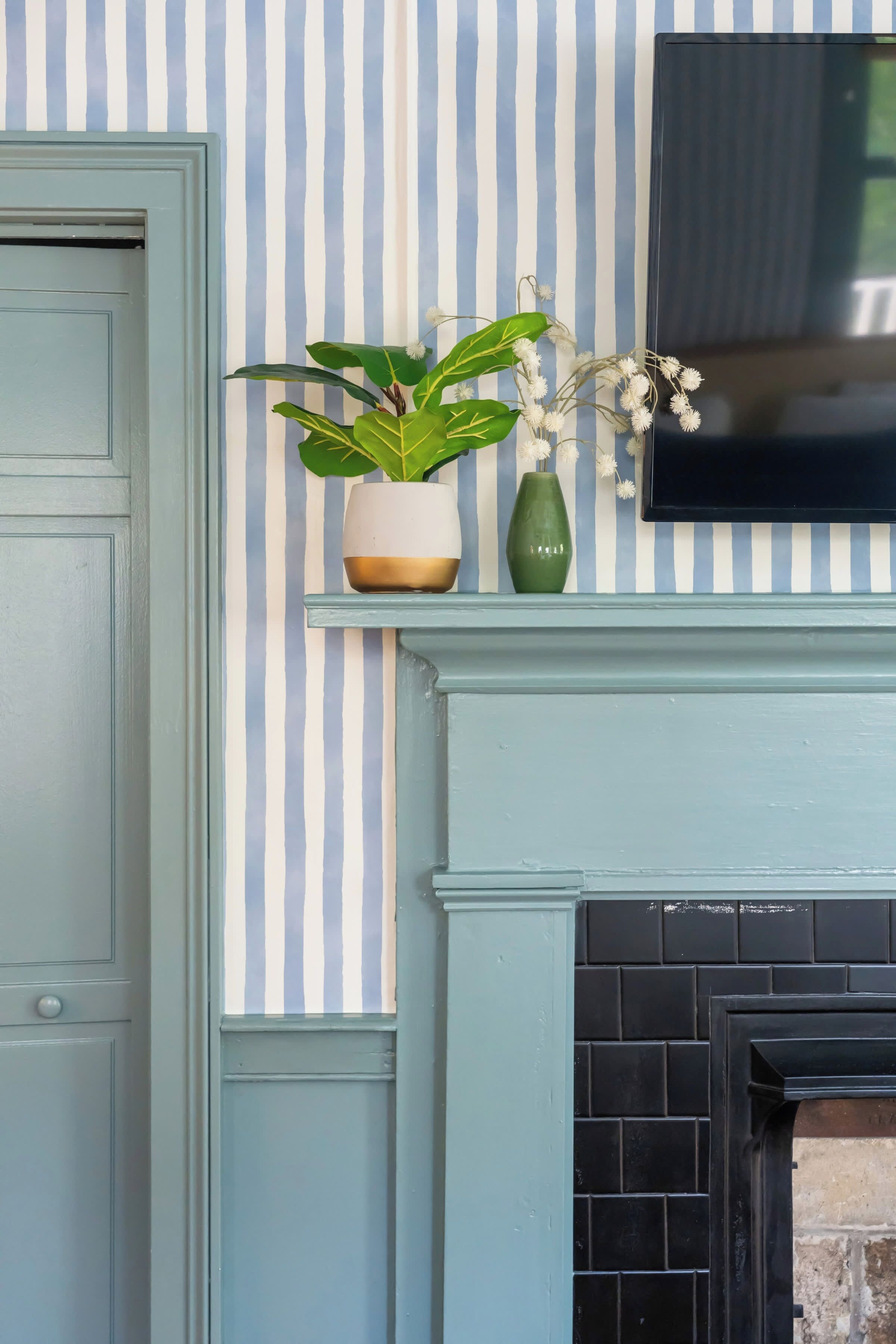 A room with a striped wall, a door, a fireplace, and a mounted television.