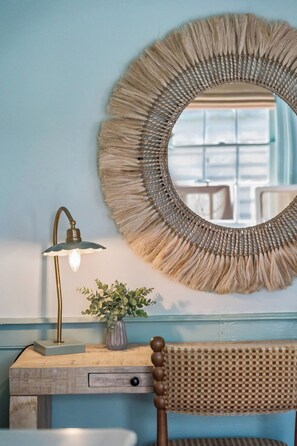A room with a round woven mirror, a desk with a lamp, and a chair. - Chic Downtown 2bd Retreat w. Parking, Perfection! (Charleston)