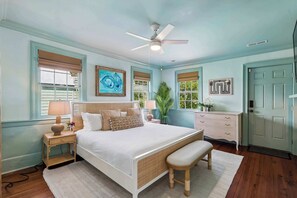 A bedroom with a bed, bedside table, lamp, bench, ceiling fan, dresser, and window with blinds.
