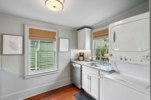 A kitchen with a dishwasher, a coffee maker, a sink, and a large white appliance, possibly a washer or dryer.