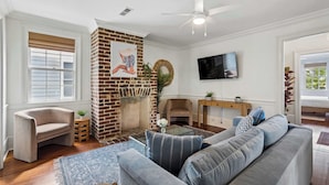 Ein Wohnzimmer mit Kamin aus Backsteinen, einem grauen Sofa, einem an der Wand befestigten Fernseher und einem Deckenventilator.