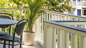 Ein überdachter Balkon mit weißer Brüstung, einem Blumentopf und einem Tisch mit Stühlen.