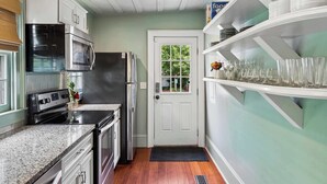 Une cuisine compacte dotée d’appareils électroménagers intégrés, une porte donnant sur un jardin et une étagère où sont rangés des verres.