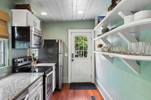 Une cuisine compacte dotée d’appareils électroménagers intégrés, une porte donnant sur un jardin et une étagère où sont rangés des verres.