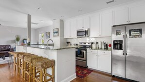 A modern kitchen with white cabinets, stainless steel appliances, and a bar area with wicker stools. - The Queens Palace | 8 Bedrooms in Charleston! (Charleston)