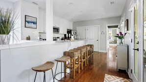 A modern kitchen with white cabinets, a central island with bar stools, and a refrigerator. - The Queens Palace | 8 Bedrooms in Charleston! (Charleston)