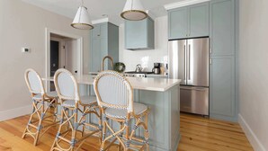Una cocina con una isla central, cuatro sillas de mimbre, un refrigerador de acero inoxidable y armarios azul claro.
