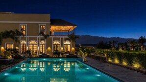 Una casa grande con piscina, ventanas arqueadas y un balcón.