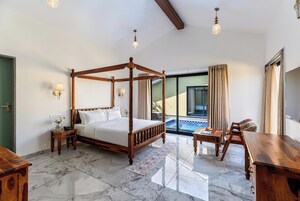 Um quarto espaçoso com uma cama de dossel, uma pequena mesa de cabeceira, uma mesa de apoio e uma escrivaninha de madeira com uma cadeira.