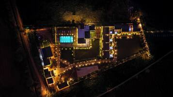 An aerial view of a resort with a swimming pool, multiple guest rooms, and well-lit pathways.