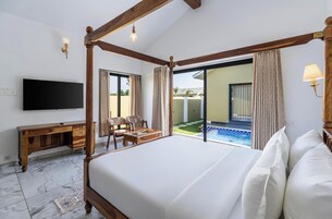 Quarto com cama de dossel, televisão, secretária de madeira e vista para uma piscina ao ar livre.