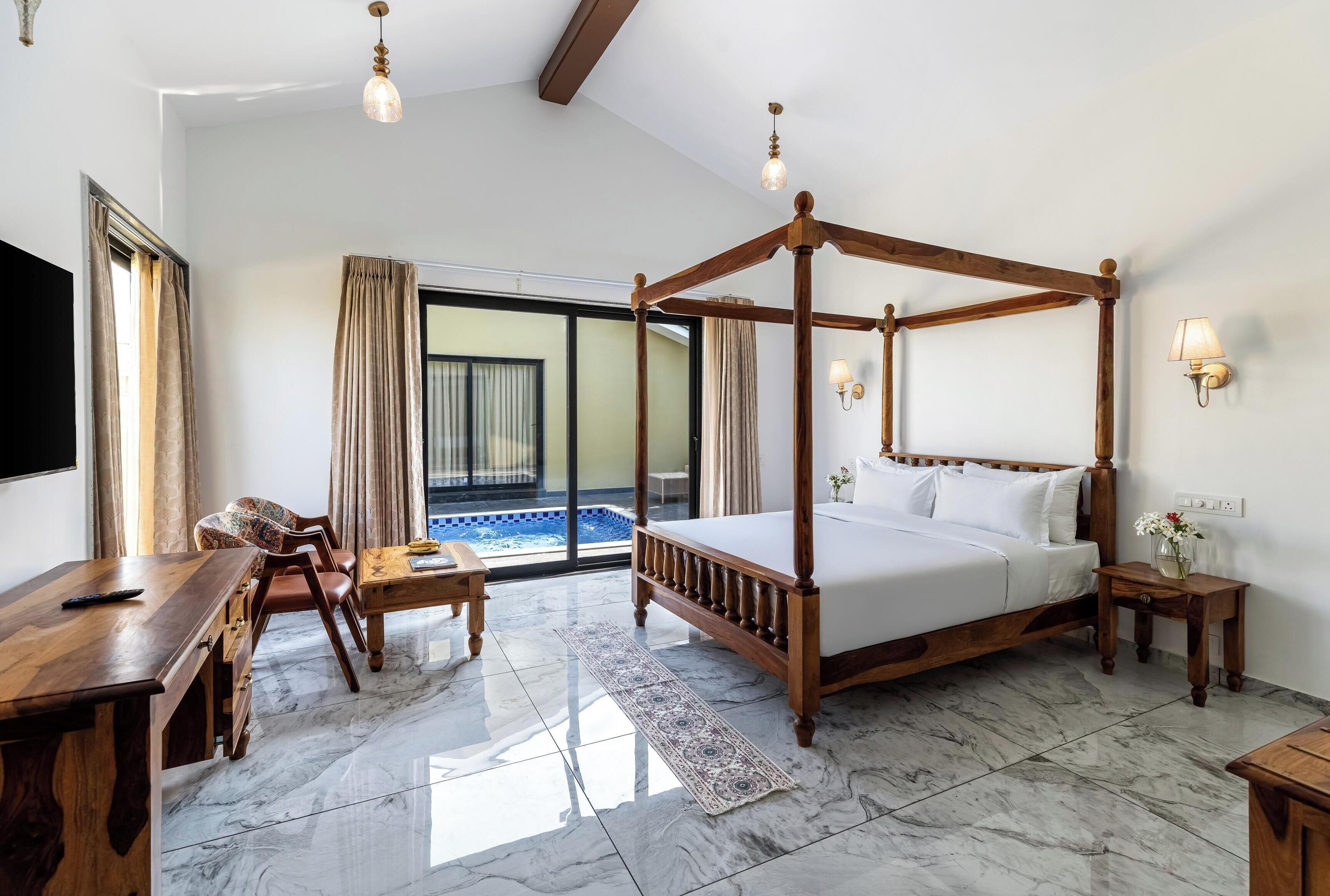 Quarto espaçoso com cama de dossel, uma escrivaninha de madeira, uma cadeira e vista para uma piscina através de uma grande janela.