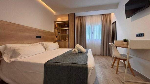Une chambre d’hôtel moderne avec un grand lit, un bureau, une chaise, une télévision et une fenêtre avec des rideaux.