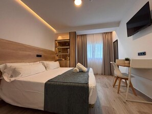 A modern hotel room with a large bed, a desk, a chair, a TV, and a window with curtains. - Hostal Hs Puerto Lumbreras  (Puerto Lumbreras)