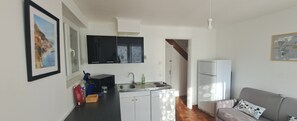 Une cuisine de taille réduite avec un plan de travail noir, des placards blancs, un évier et une cuisinière. On y trouve également un réfrigérateur, un four à micro-ondes et une porte qui donne sur une autre pièce.