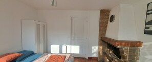 Une chambre avec un lit, une armoire, une cheminée en briques et une porte.