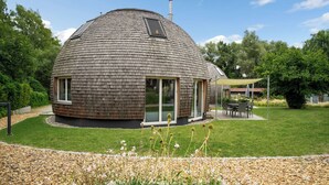 A dome-shaped house with a chimney, a patio with a table and chairs, and a garden with flowers and gravel. - Vacation home "Eos" on Lake Tollensesee in Penzlin Wustrow (Penzlin)