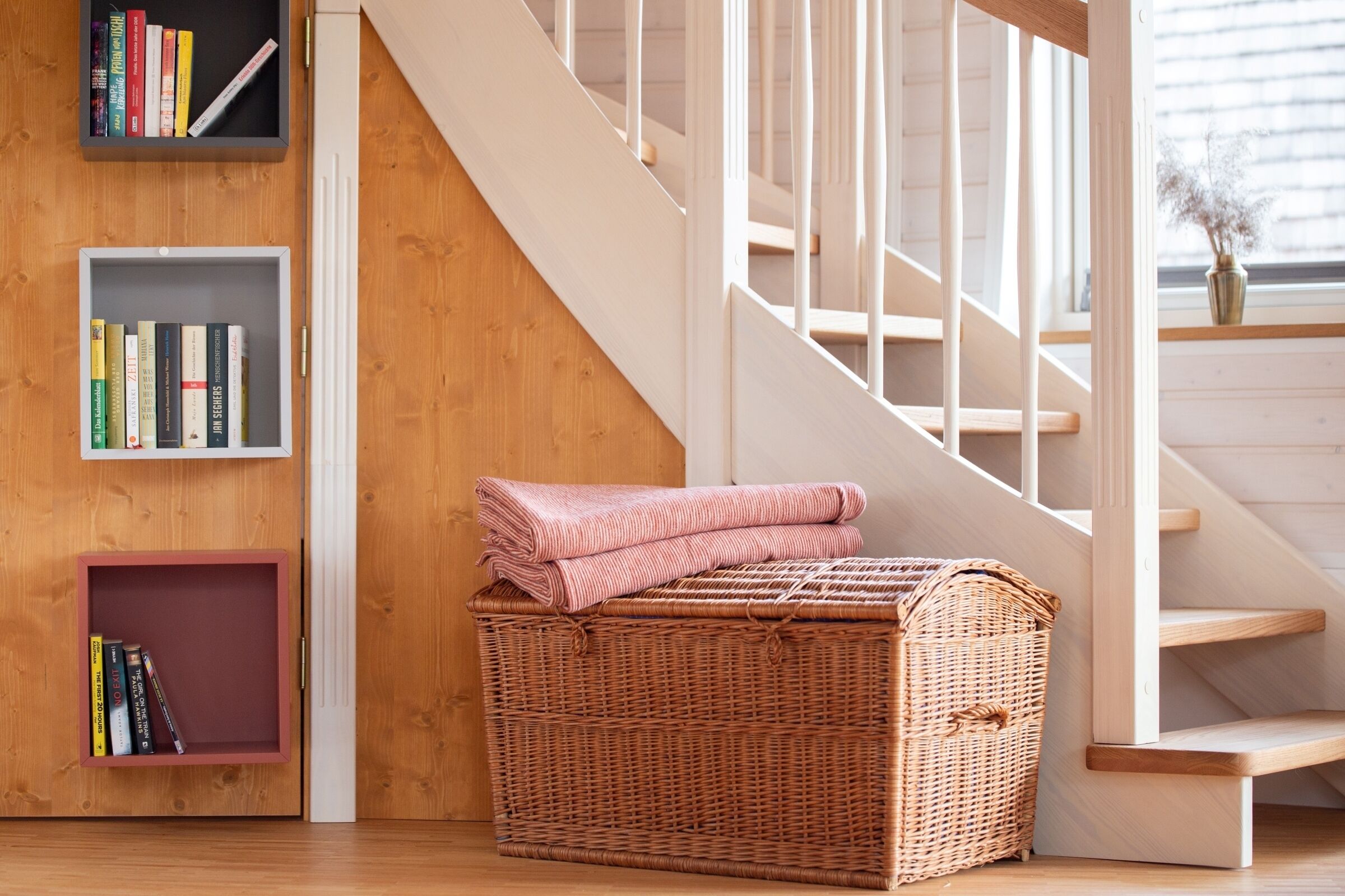 Eine Holztreppe, ein Korbwesen und Bücherregale mit Büchern.
