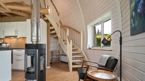 A modern kitchen with a wood-burning stove, a dining area with a round table and chairs, and a staircase leading to an upper level. - Vacation home "Phoebe" on Lake Tollensesee in Penzlin Wustrow (Penzlin)